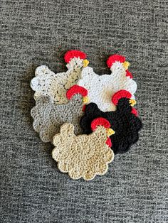 three crocheted chicken coasters sitting on top of a gray carpeted floor