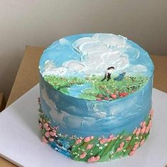 there is a blue cake with flowers and clouds on the top, sitting on a cardboard box