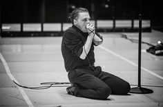 a man sitting on the ground with his hands in his mouth while holding a microphone