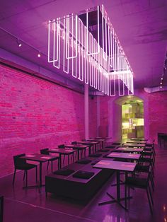 an empty dining room with tables and chairs in front of a brick wall that has neon lights hanging from the ceiling