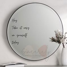 a round mirror with writing on it next to a vase