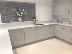 a kitchen with white cabinets and gray counter tops is pictured in this image, there are vases on the window sill