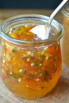 a jar filled with soup sitting on top of a wooden table next to a spoon