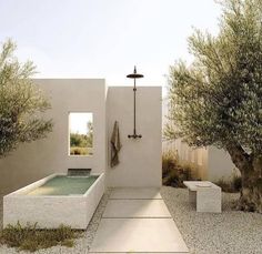 an outdoor shower with two trees and a bench in the foreground, next to a pool