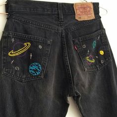 a pair of black jeans with embroidered planets and stars on the back, sitting on a white surface