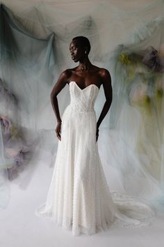 a woman standing in front of a white backdrop wearing a dress with flowers on it