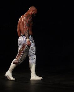 a man in white boots and wrestling gear walking with his leg wrapped around an object