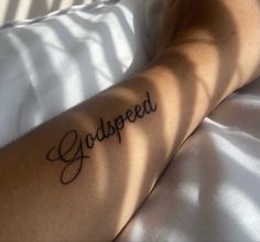 a person laying in bed with a tattoo on their arm that reads, godspeed