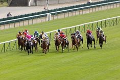 several jockeys are riding their horses down the track at a horse racing event in an open field