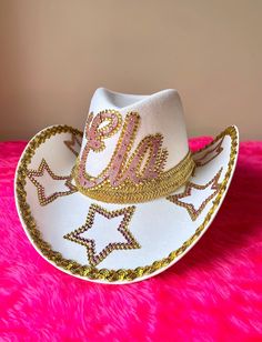 A white cowboy hat embellished with pink and gold rhinestone stars and personalised with your chosen name, initials, numbers or symbol The final touch to your rhinestone cowgirl look Festival season necessity One size fits all - These hats have an approx circumference of 58cm (chin strap string to fasten safely perfect for table top dancing) Contact me for any personalisation requests FREE UK DELIVERY Badazzel Cowboy Hat, Bedazzled Cowboy Hat, Decorated Cowboy Hats, Star Cowboy Hat, Look Cowgirl, Rhinestone Cowgirl Hat, Cute Party Outfits, Childrens Fancy Dress, White Cowboy Hat