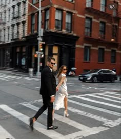 a man and woman walking across a crosswalk in the middle of a city street