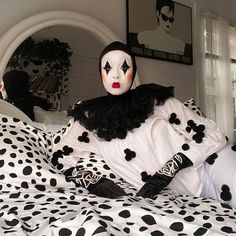 a person with white and black makeup sitting on a polka dot bed in a bedroom