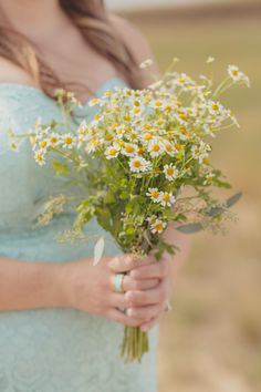 a woman in a blue dress holding a bouquet of daisies and wildflowers