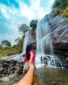 a person standing in front of a waterfall with their hand on the water's edge