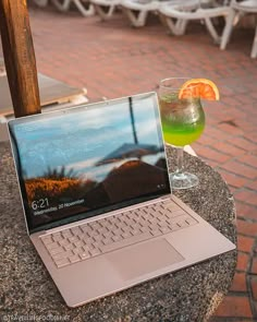 an open laptop computer sitting on top of a table next to a glass filled with liquid