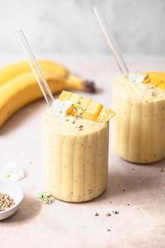 two glasses filled with smoothie next to bananas and spoons on a counter top