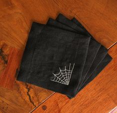 four black napkins with white spider web on them sitting on a wooden table top