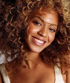 a close up of a woman with curly hair smiling and wearing a white tank top