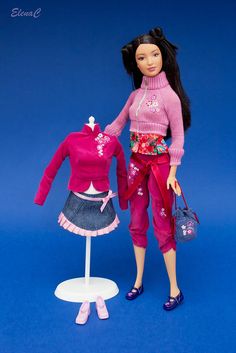 a barbie doll standing next to a dress and purse