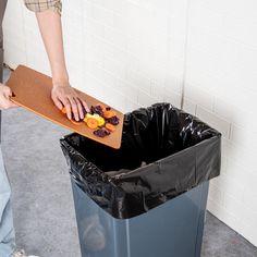 a person holding a cutting board over a trash can