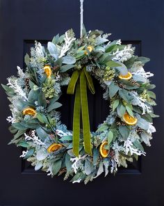 a wreath on the front door is decorated with oranges and greenery, while green ribbon hangs from it