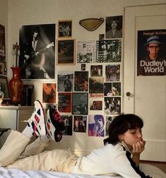 a woman laying on top of a bed next to a wall covered in pictures and posters