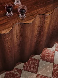 two wine glasses sitting on top of a wooden table next to a red and white checkered floor