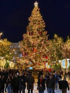 many people are walking in front of a christmas tree