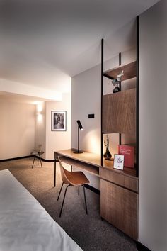 a hotel room with a bed, desk and chair next to a wall mounted book shelf