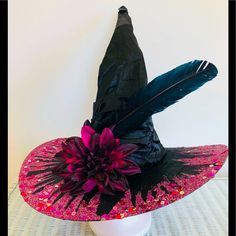 a black hat with pink flowers and feathers on top of a white table next to a wall