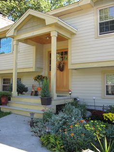 the front porch of a house with flowers and plants in pots on the steps leading up to it