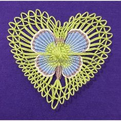 a blue and green heart shaped brooch on a purple background with white stitching