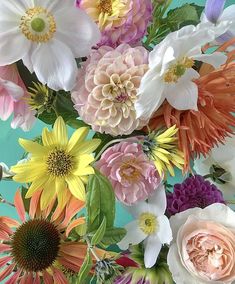 an arrangement of colorful flowers in a vase on a blue tablecloth, with one large flower surrounded by smaller ones