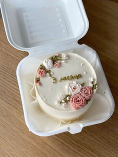 a white cake with pink flowers in a plastic container