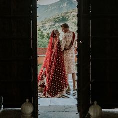 a bride and groom standing in an open doorway with mountains in the background at their wedding