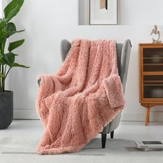 a pink blanket sitting on top of a gray chair next to a potted plant