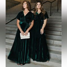 two women in green velvet dresses standing on stairs