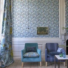 two chairs and a table in front of a wall with blue floral designs on it