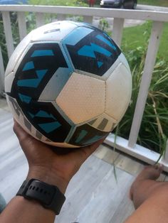 a person holding up a soccer ball in their hand on a porch with grass and bushes