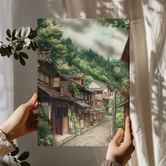 a person holding up a painting in front of a window with trees and buildings on it