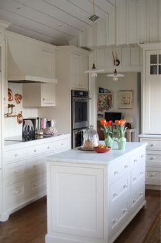 a large kitchen with white cabinets and an island in the middle is decorated with tulips