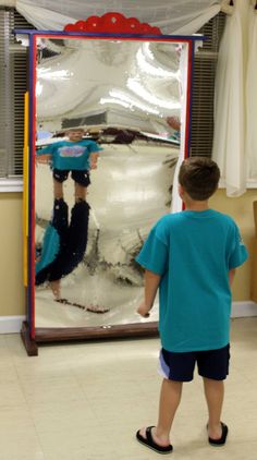 a young boy standing in front of a mirror reflecting another person's reflection on the wall