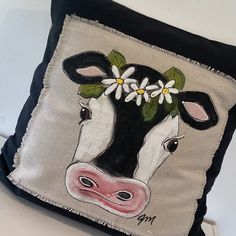 a black and white pillow with a cow's face painted on the front, surrounded by daisies