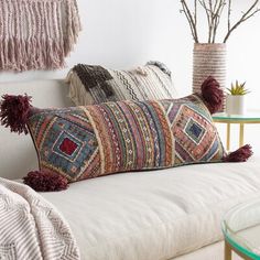 a couch with two pillows on it and some plants in vases next to it