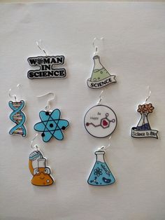 six different science themed earrings on a white surface with the words woman in science printed on them