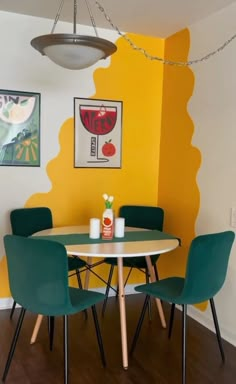 a dining room table with green chairs next to a yellow wall and pictures on the wall