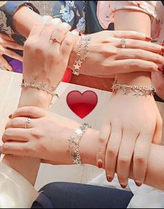 two hands holding onto each other while wearing bracelets with hearts on them and one has a red heart in the middle