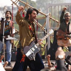 a man with a guitar in his hand and other people behind him playing music on stage