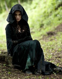 a woman dressed in black sitting on the ground with a hood over her head and eyes closed