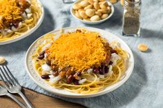 two plates of spaghetti with beans, cheese and nuts on a table next to silverware